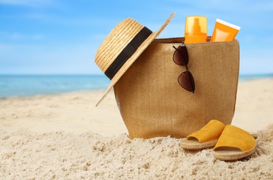 Stylish bag with different accessories on sandy beach near ocean