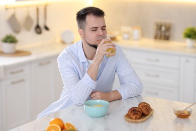 Photo of Handsome man drinking juice at breakfast indoors
