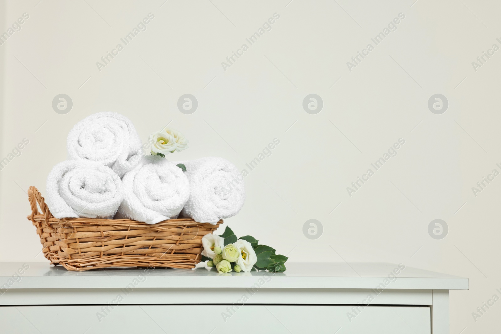 Photo of Soft folded towels and flowers on white table, space for text