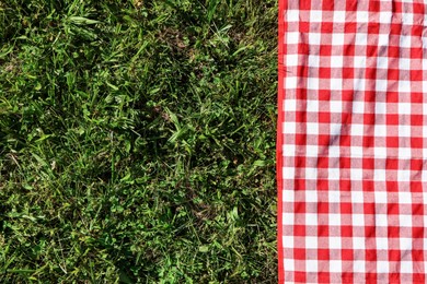 Photo of Checkered picnic tablecloth on fresh green grass, top view. Space for text