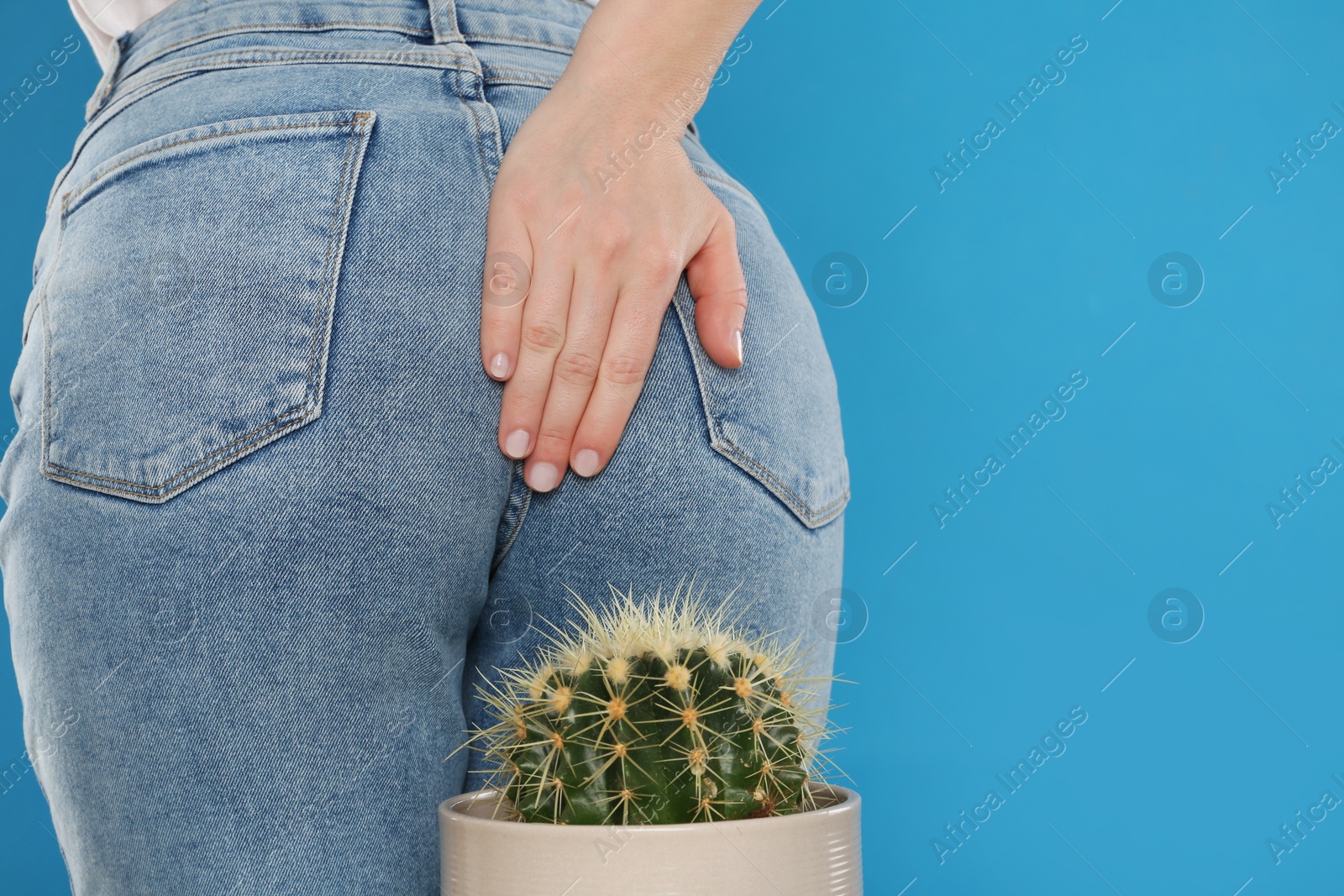 Photo of Woman sitting down on cactus against light blue background, space for text. Hemorrhoid concept