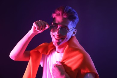 Stylish young man in sunglasses on dark background in neon lights