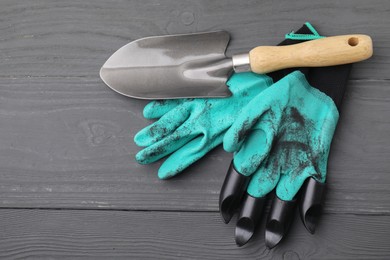 Photo of Pair of claw gardening gloves and trowel on grey wooden table, top view. Space for text