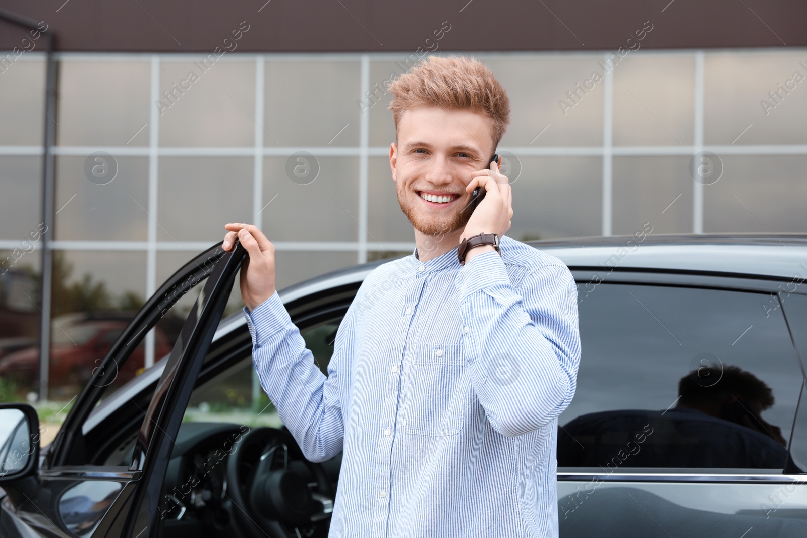 Photo of Attractive young man talking on phone near car outdoors