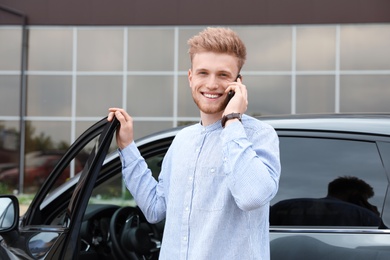 Photo of Attractive young man talking on phone near car outdoors