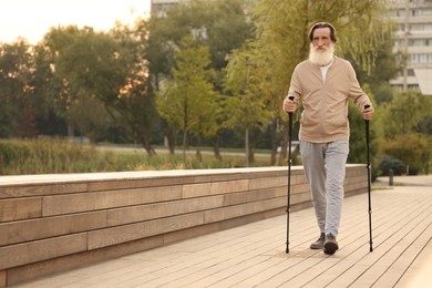 Photo of Senior man performing Nordic walking outdoors, space for text