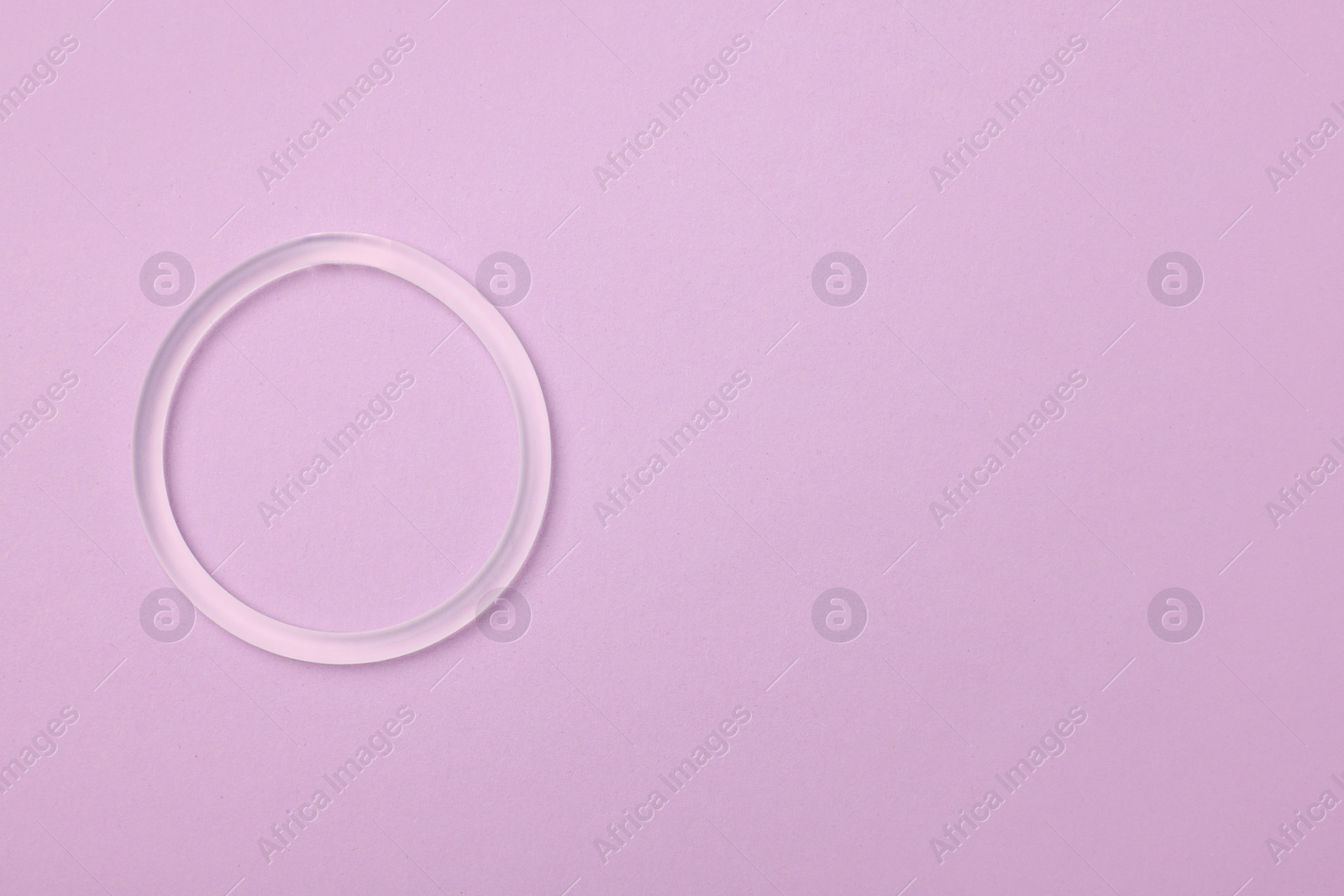 Photo of Diaphragm vaginal contraceptive ring on lilac background, top view. Space for text