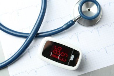 Modern fingertip pulse oximeter, stethoscope and cardiogram on grey table, flat lay