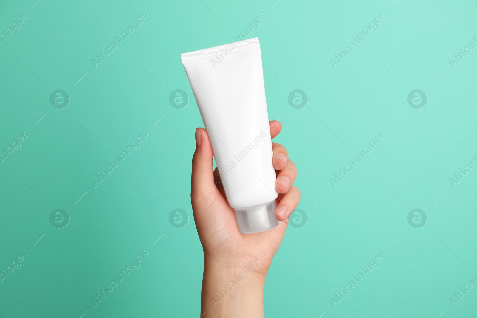 Photo of Woman holding tube of face cream on turquoise background, closeup