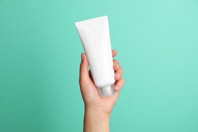 Photo of Woman holding tube of face cream on turquoise background, closeup