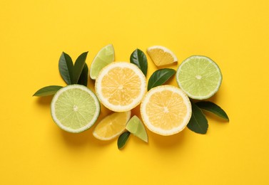 Photo of Fresh ripe lemons, limes and green leaves on yellow background, flat lay