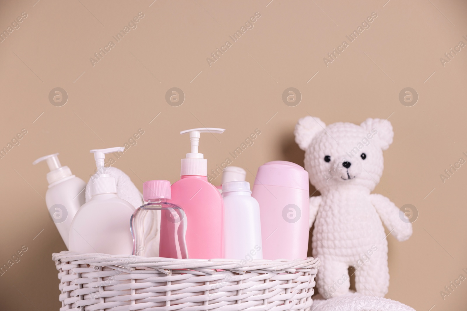 Photo of Wicker basket with baby cosmetic products and knitted toy bear on beige background