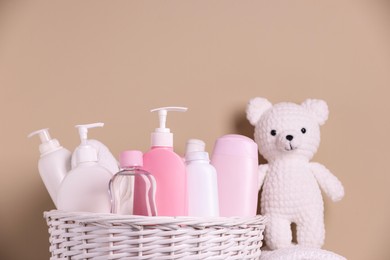 Wicker basket with baby cosmetic products and knitted toy bear on beige background