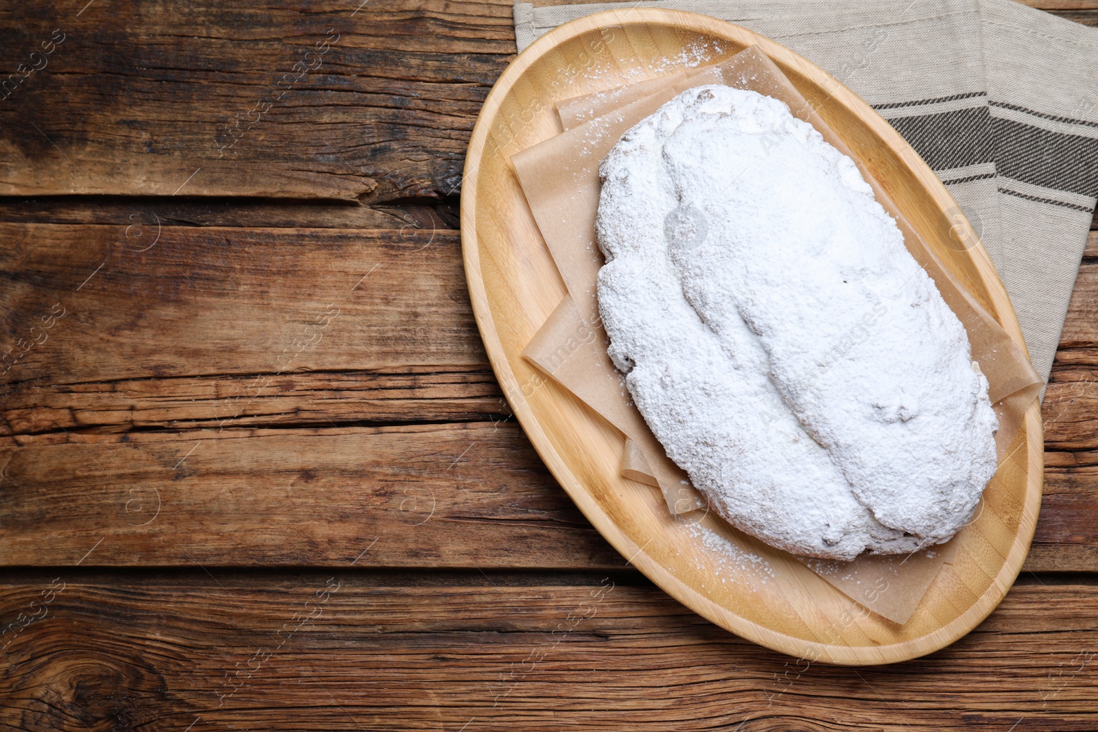 Photo of Plate of delicious Stollen sprinkled with powdered sugar on wooden table, top view. Space for text