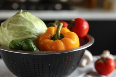 Metal colander with different wet vegetables on white textured table, closeup