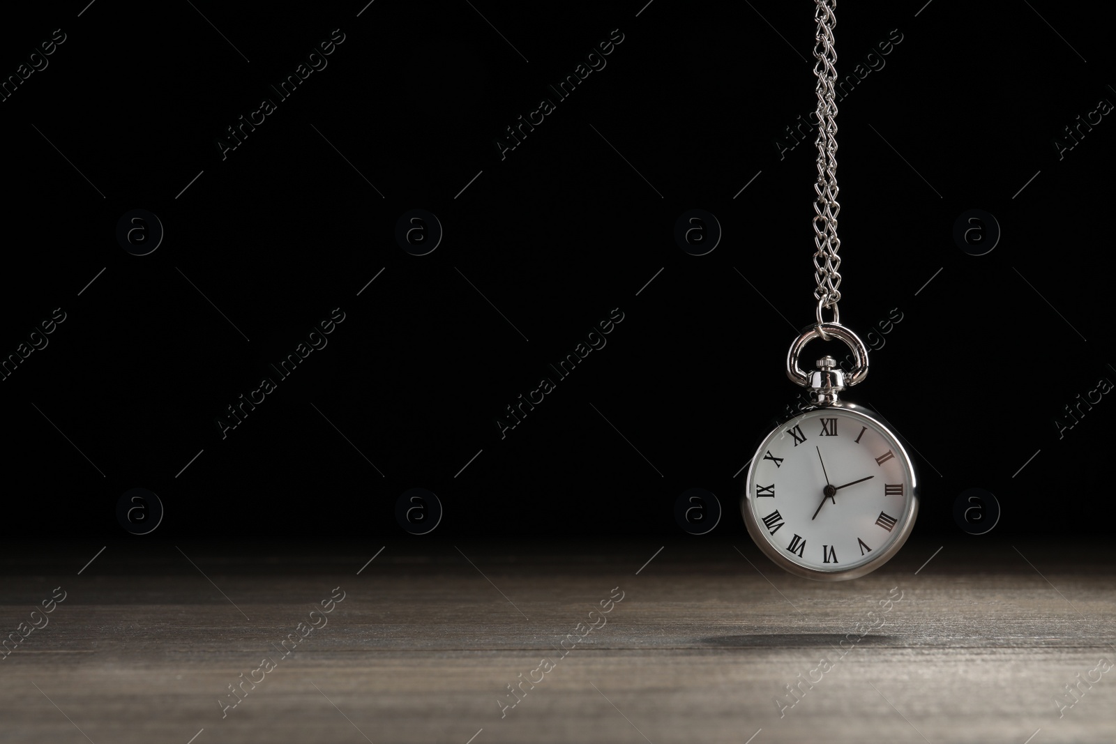 Photo of Beautiful vintage pocket watch with silver chain on black background above wooden table, space for text. Hypnosis session