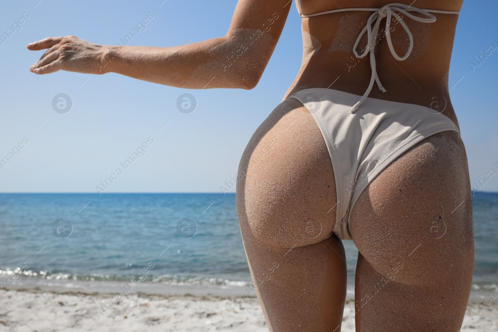 Photo of Woman with sand on perfect body in bikini near sea, closeup. Back view