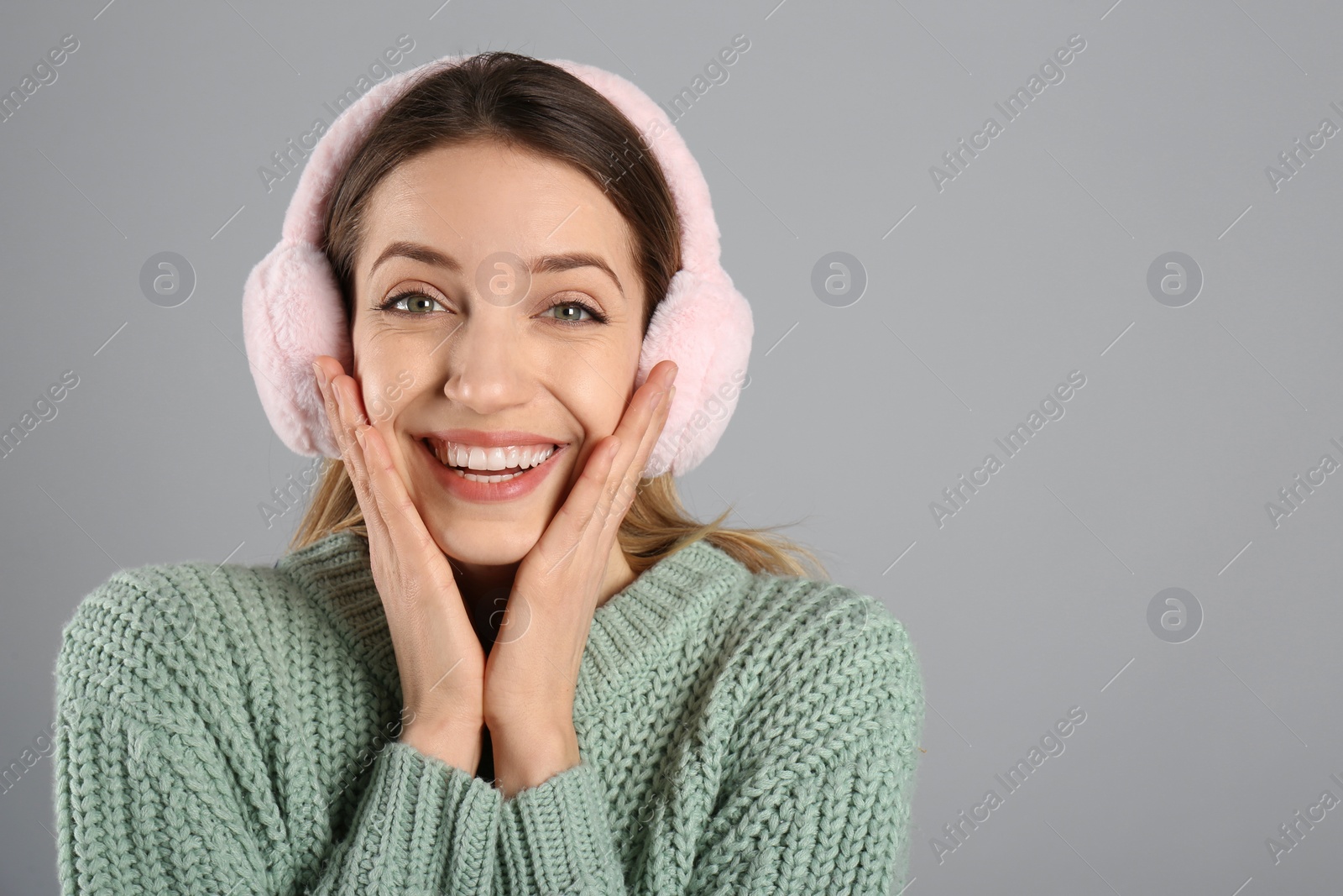 Photo of Happy woman wearing warm earmuffs on grey background, space for text