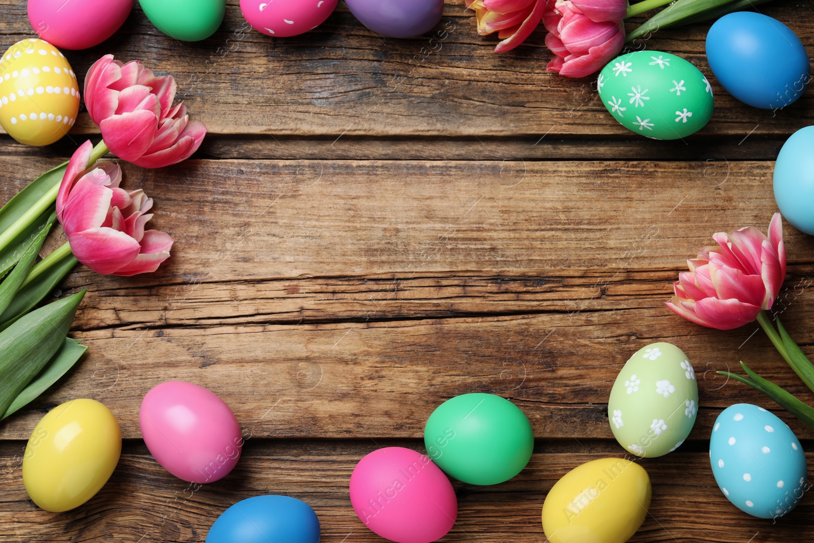 Photo of Frame of colorful eggs and tulips on wooden background, flat lay with space for text. Happy Easter