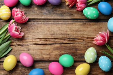 Frame of colorful eggs and tulips on wooden background, flat lay with space for text. Happy Easter