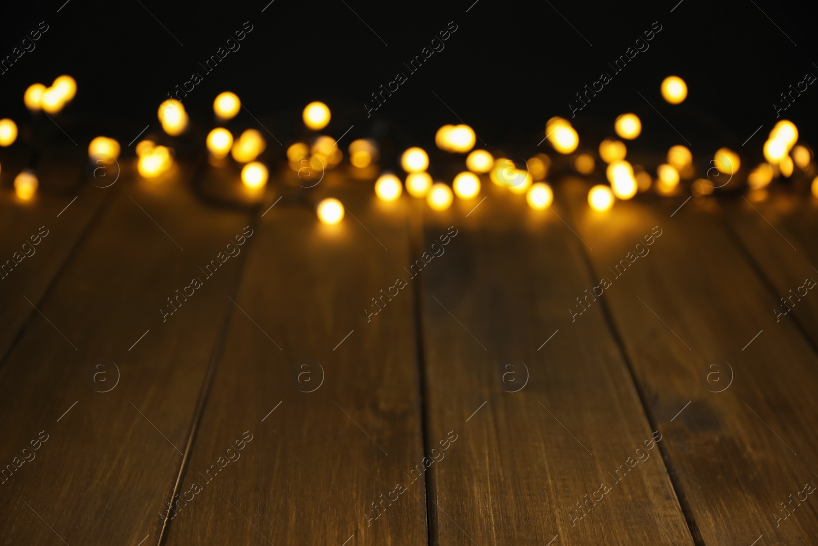 Photo of Blurred view of beautiful glowing lights, focus on wooden table. Space for text