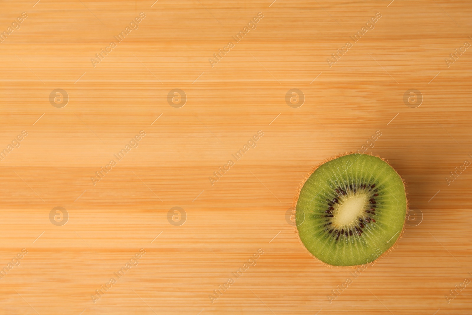 Photo of Half of fresh ripe kiwi on wooden table, top view. Space for text