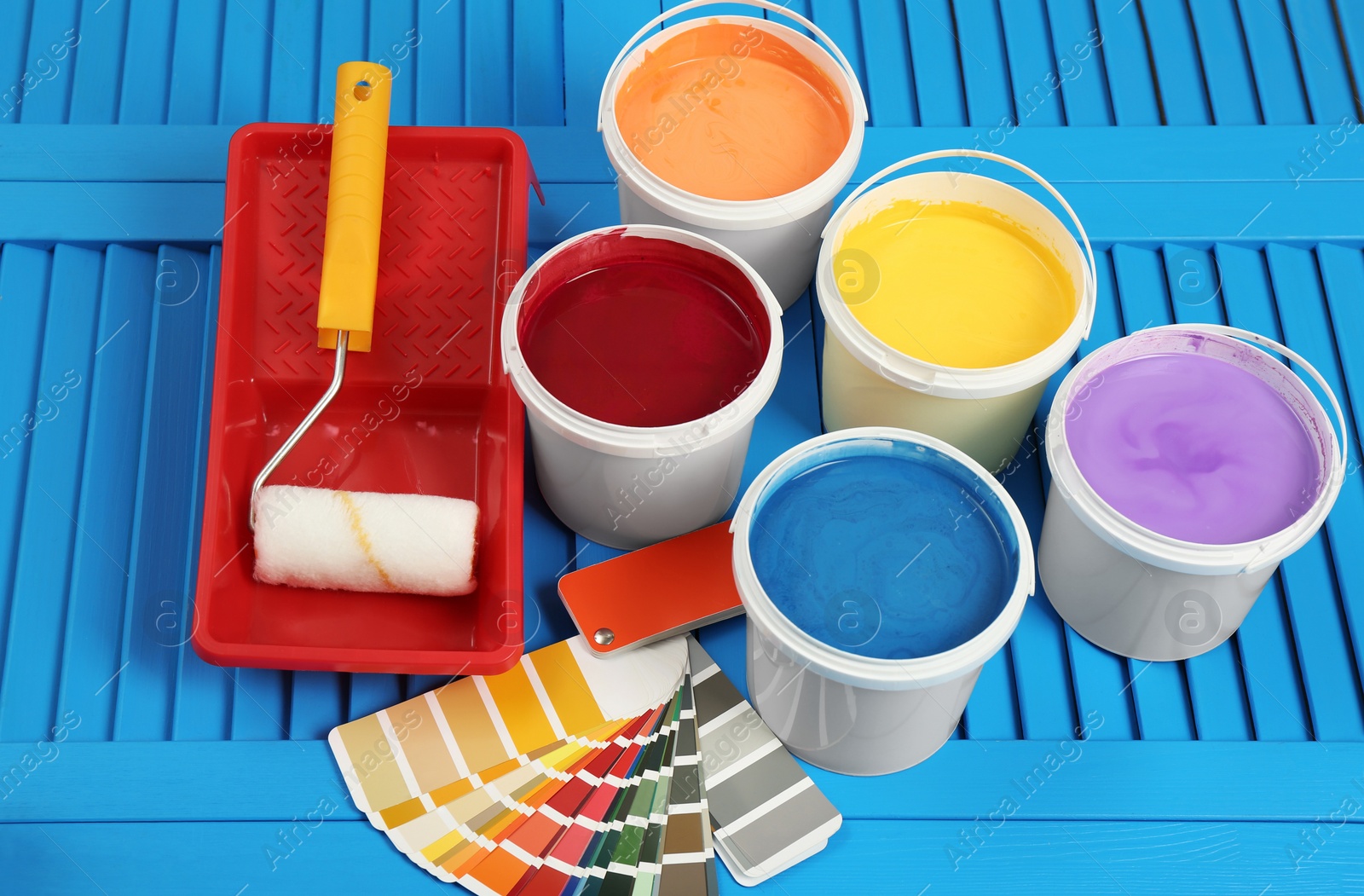 Photo of Buckets of paints, palette and decorator's tools on light blue wooden background, above view