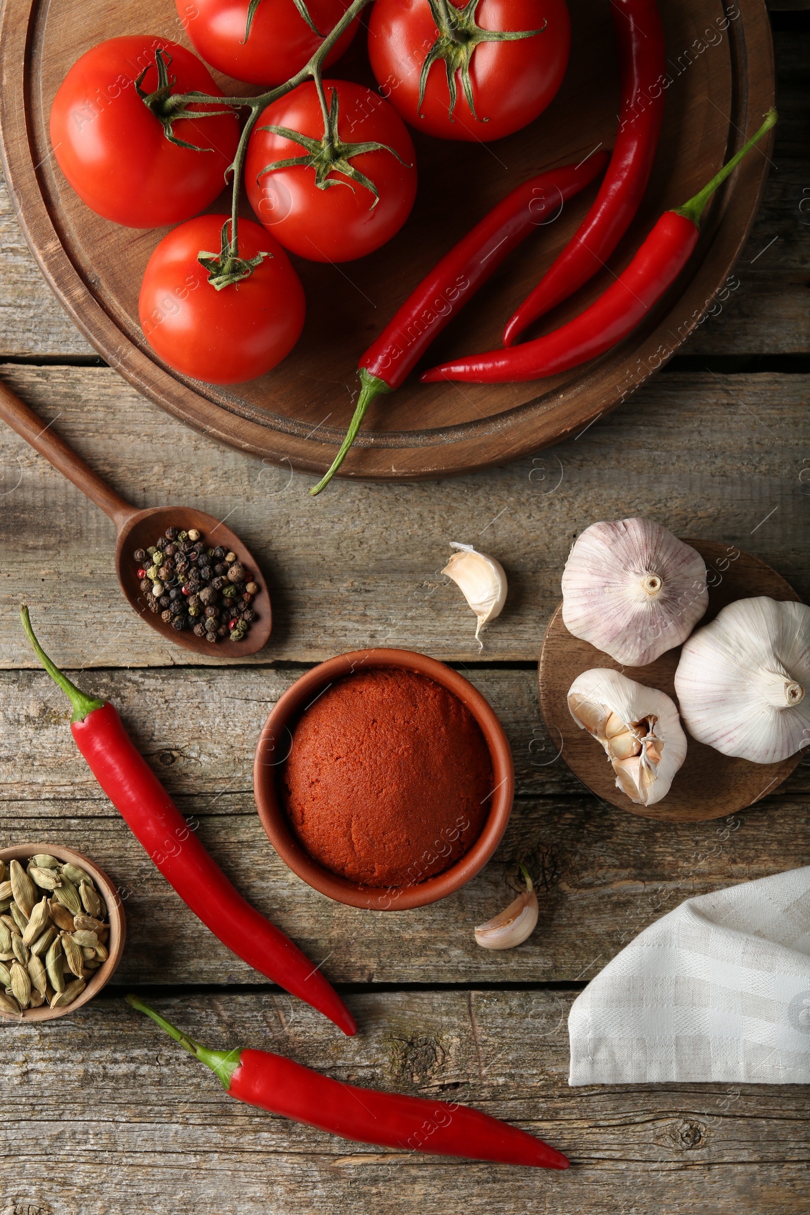 Photo of Red curry paste in bowl and ingredients on wooden table, flat lay