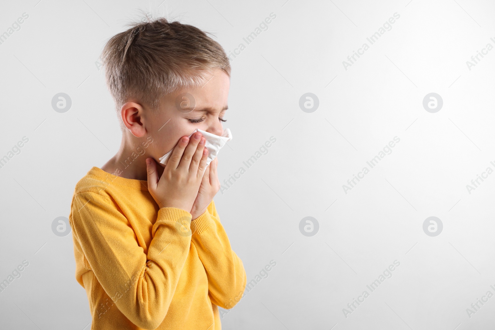 Photo of Sick boy with tissue coughing on gray background, space for text. Cold symptoms