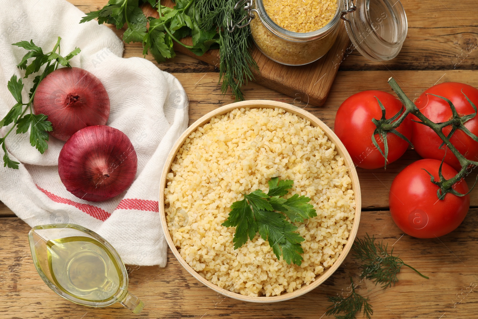 Photo of Delicious bulgur with parsley, onion, oil and tomatoes on wooden table, flat lay