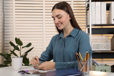 Photo of Happy woman taking sticky note at table in office