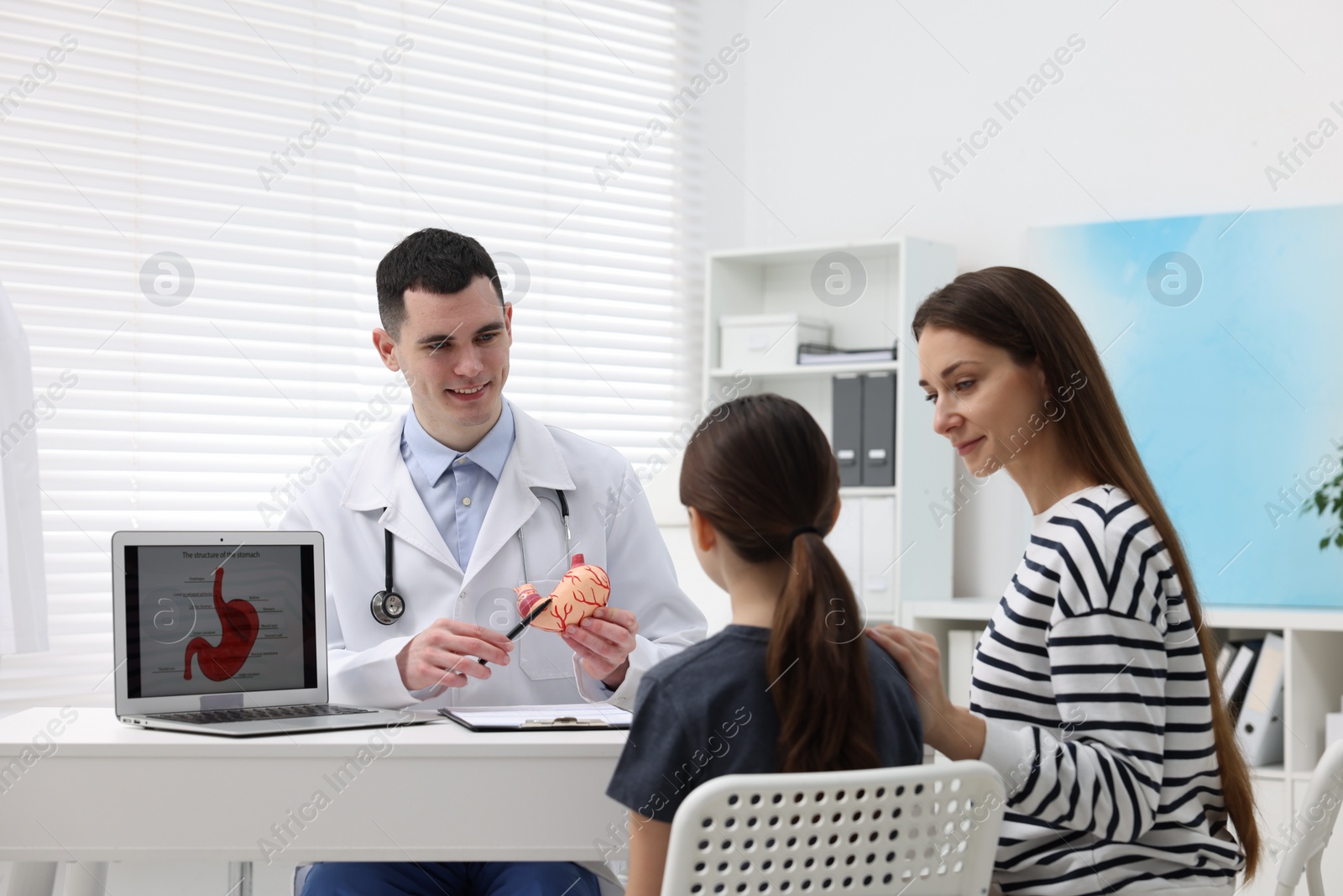 Photo of Gastroenterologist with model of stomach consulting woman and her daughter in clinic