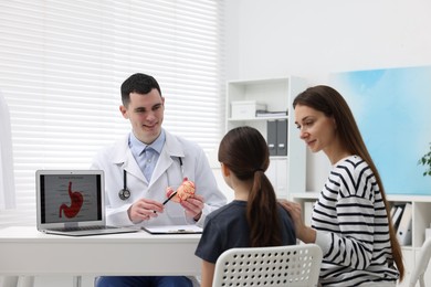 Gastroenterologist with model of stomach consulting woman and her daughter in clinic