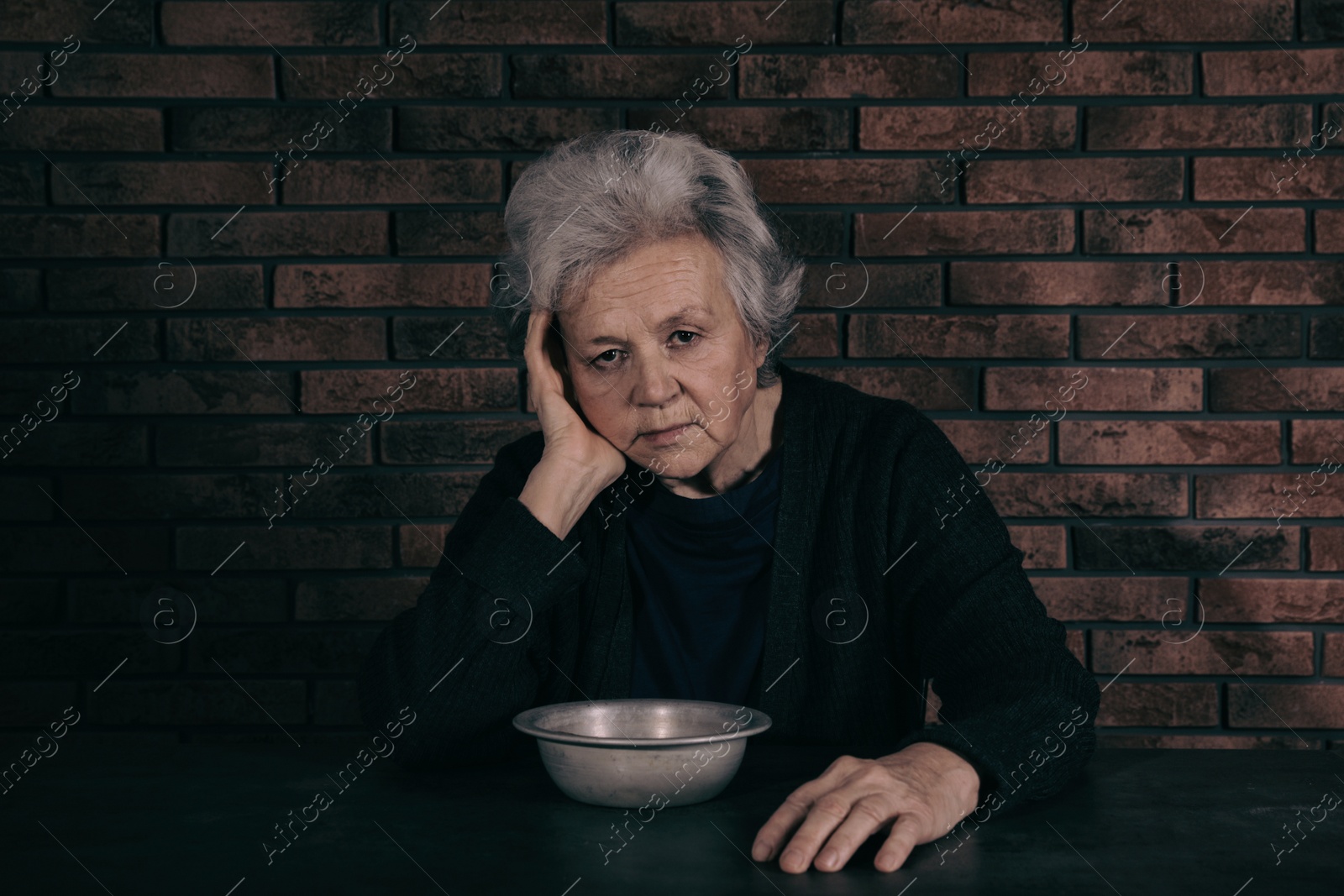 Photo of Poor mature woman with bowl sitting at table