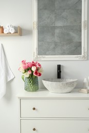 Vase with beautiful pink tulips and toiletries near sink in bathroom