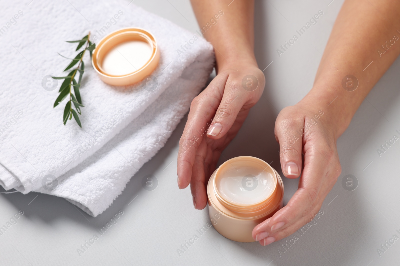 Photo of Woman with jar of hand cream, towel and green twig on light grey background, closeup