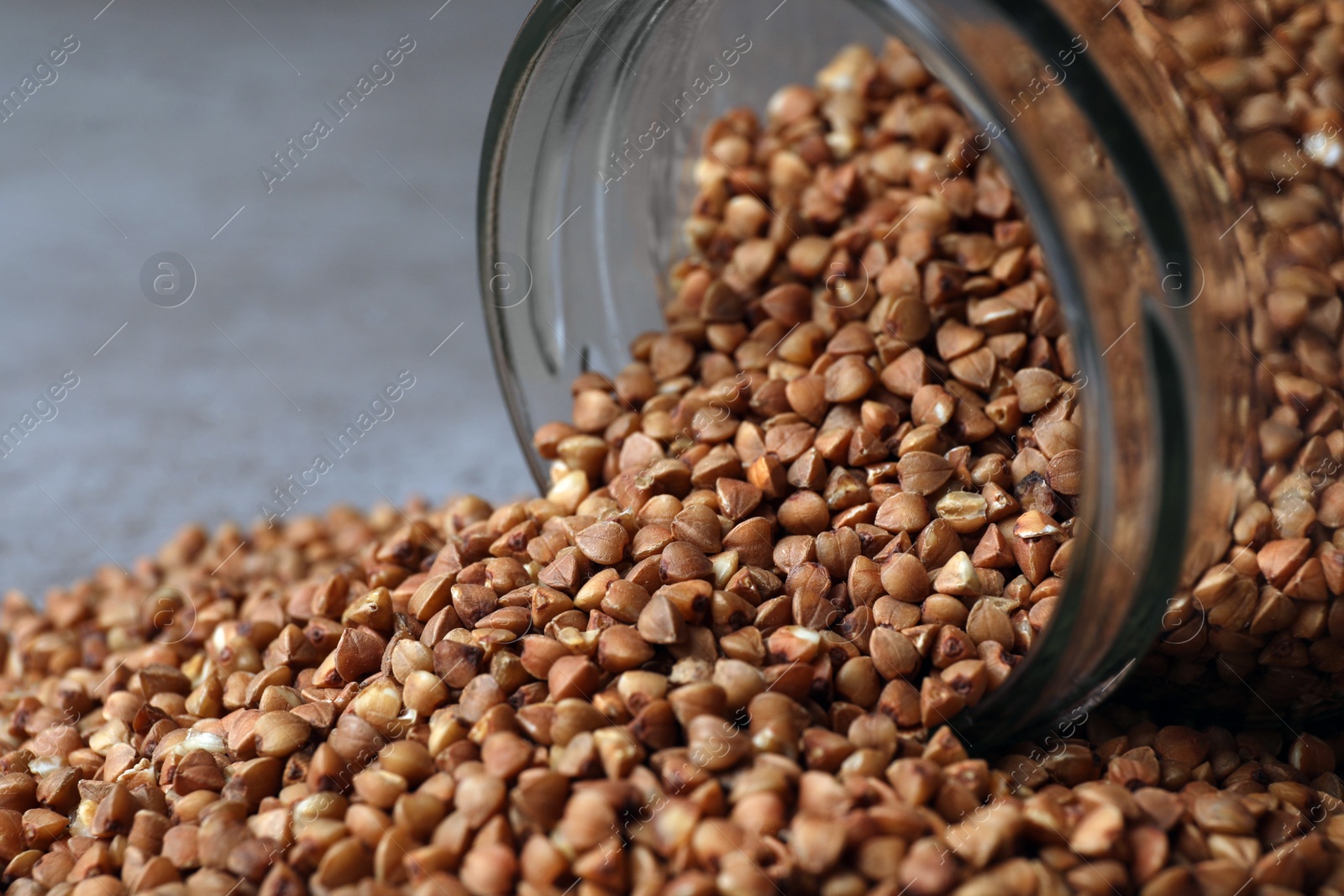 Photo of Overturned glass jar with uncooked buckwheat on table, closeup