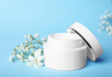 Jar of luxury face cream and flowers on light blue background