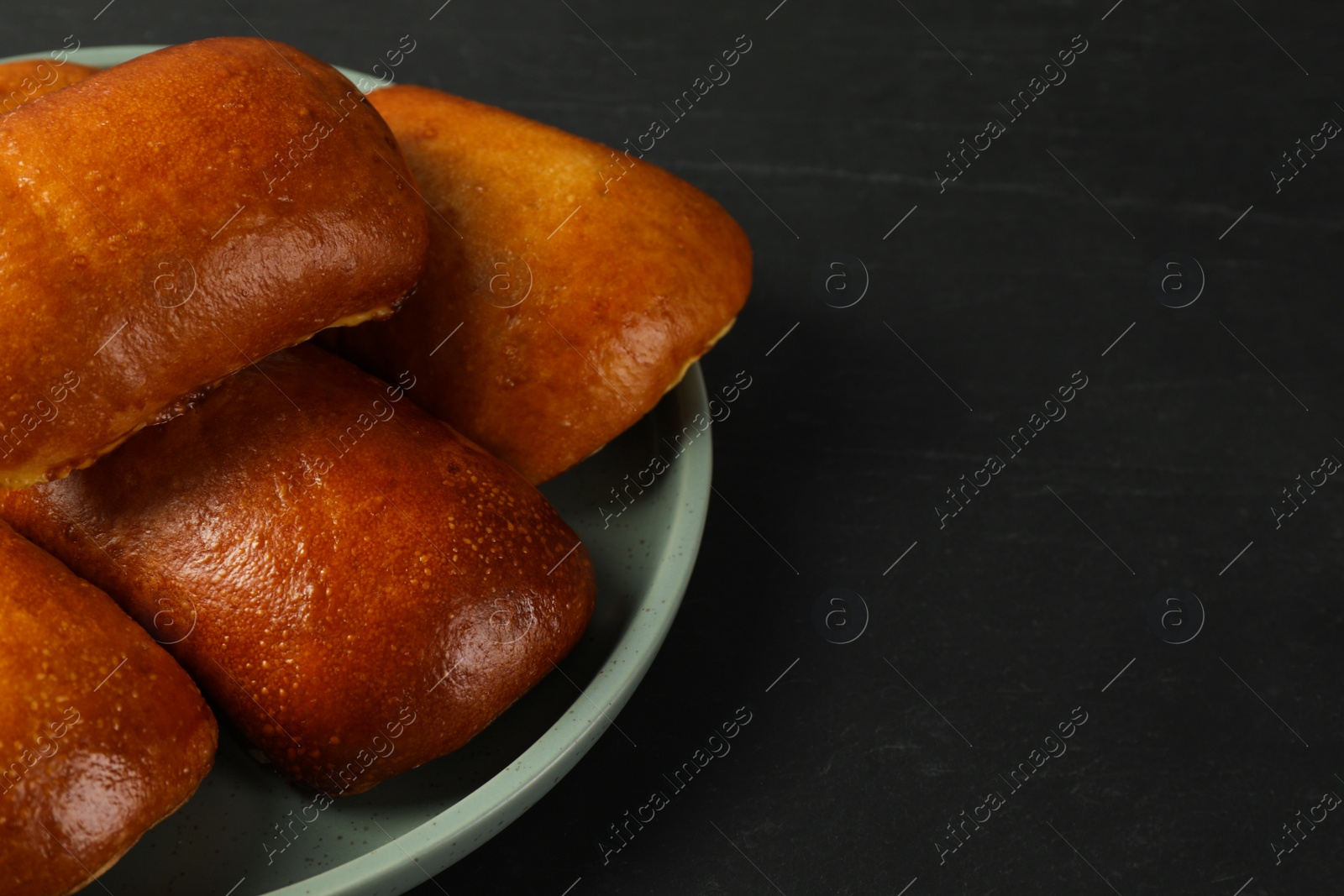 Photo of Delicious baked pirozhki on black table, closeup. Space for text