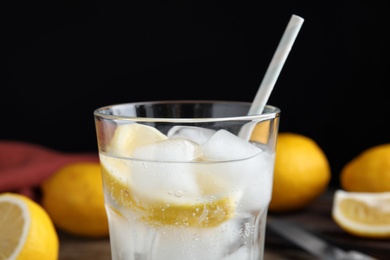 Soda water with lemon slices and ice cubes on black background, closeup