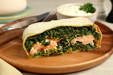 Piece of delicious strudel with salmon and spinach served on wooden table, closeup