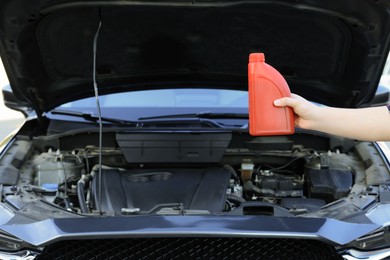 Man holding bottle of motor oil near car, closeup. Space for text