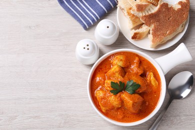 Bowl of delicious chicken curry on white wooden table, flat lay. Space for text