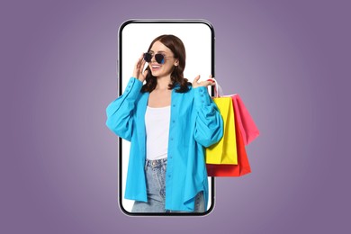 Online shopping. Happy woman with paper bags looking out from smartphone on violet background