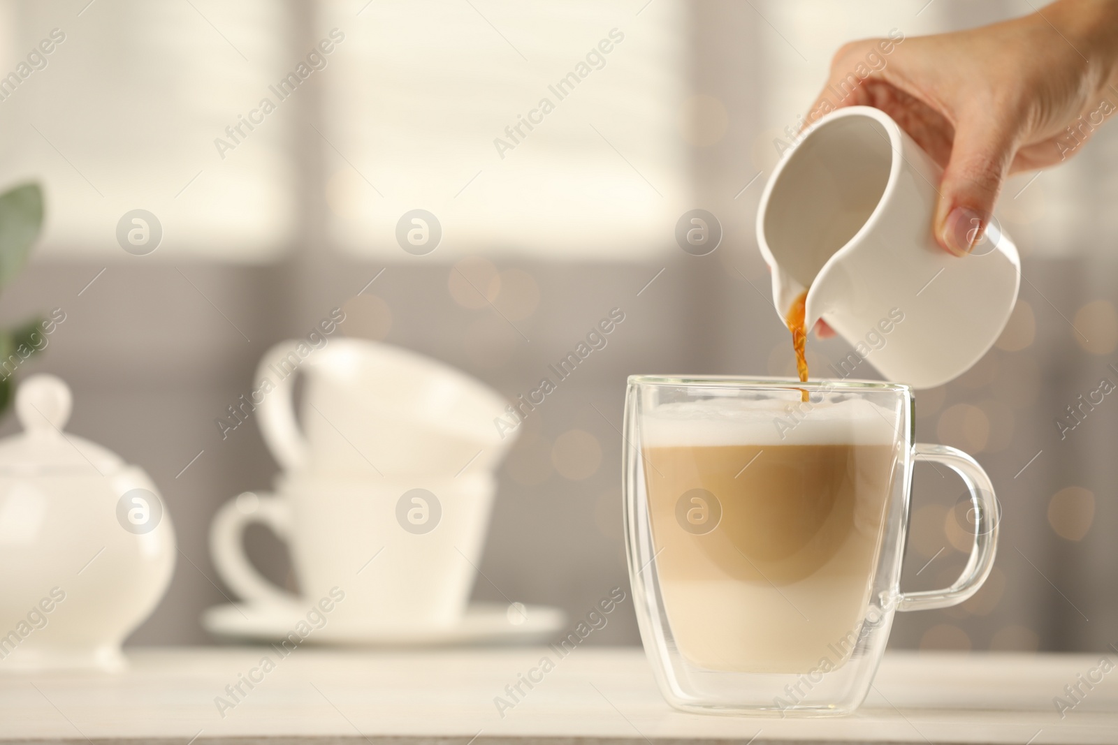 Photo of Woman pouring coffee into cup with milk at table indoors, closeup