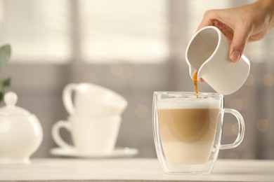 Photo of Woman pouring coffee into cup with milk at table indoors, closeup