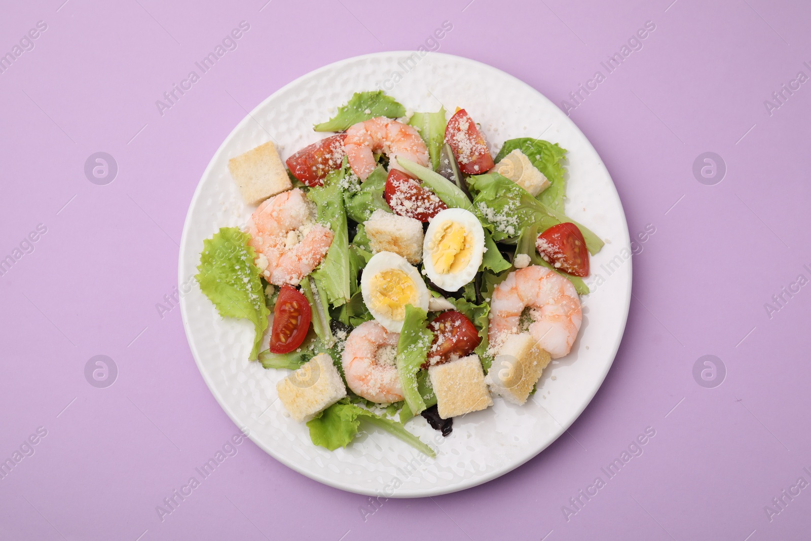 Photo of Delicious Caesar salad with shrimps on violet background, top view