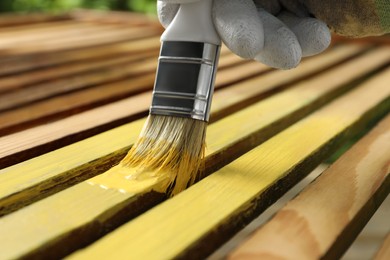 Photo of Worker painting wooden surface with yellow dye outdoors, closeup