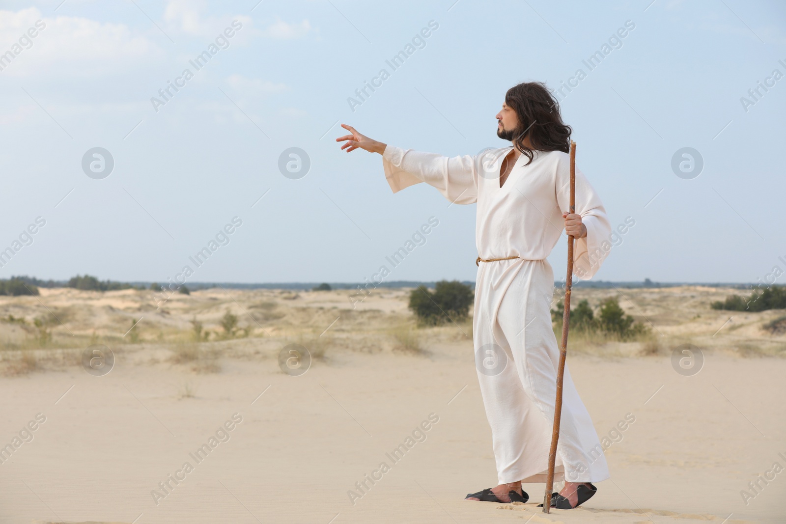 Photo of Jesus Christ walking with stick in desert. Space for text