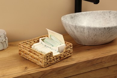 Photo of Wicker basket with different tampons on wooden countertop in bathroom. Menstrual hygienic product